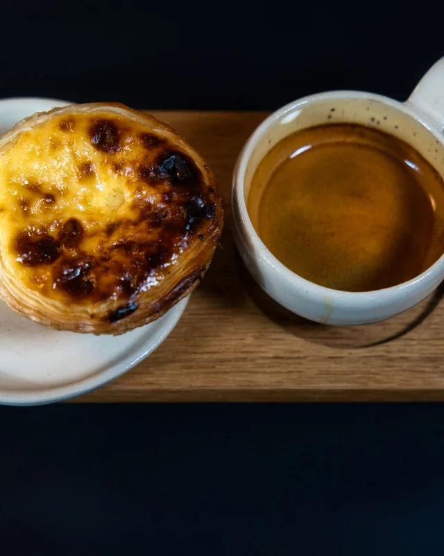 ‏طاولة في Café Lisboa عليها إسبريسو وPastel de Nata